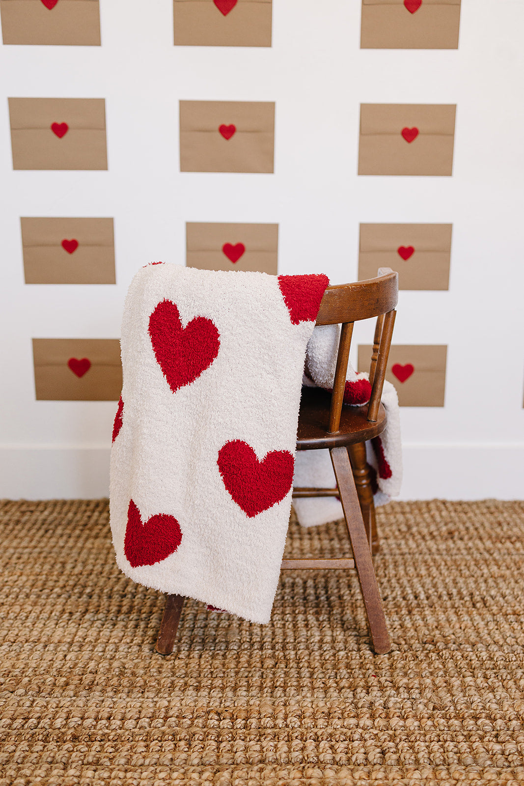 White blanket with red heart patterns draped over a wooden chair against a wall with heart decorations.