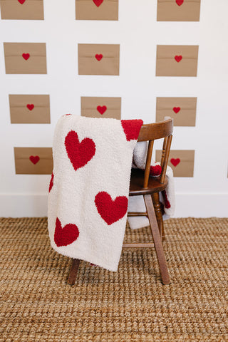 White blanket with red heart patterns draped over a wooden chair against a wall with heart decorations.