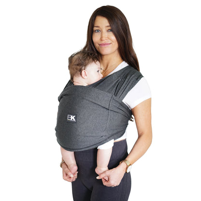 A woman wearing a heather black Baby K'tan Active Yoga Baby Carrier with a sleeping infant inside it.