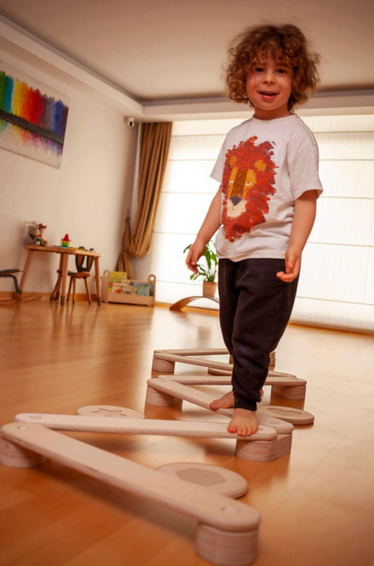 Child standing on a wooden balance beam in a room with colorful decorations.