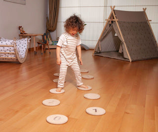Child playing with number cards on a wooden floor in a room with a teepee and crib.
