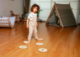 Child standing on numbered stepping stones in a room with a teepee and crib.