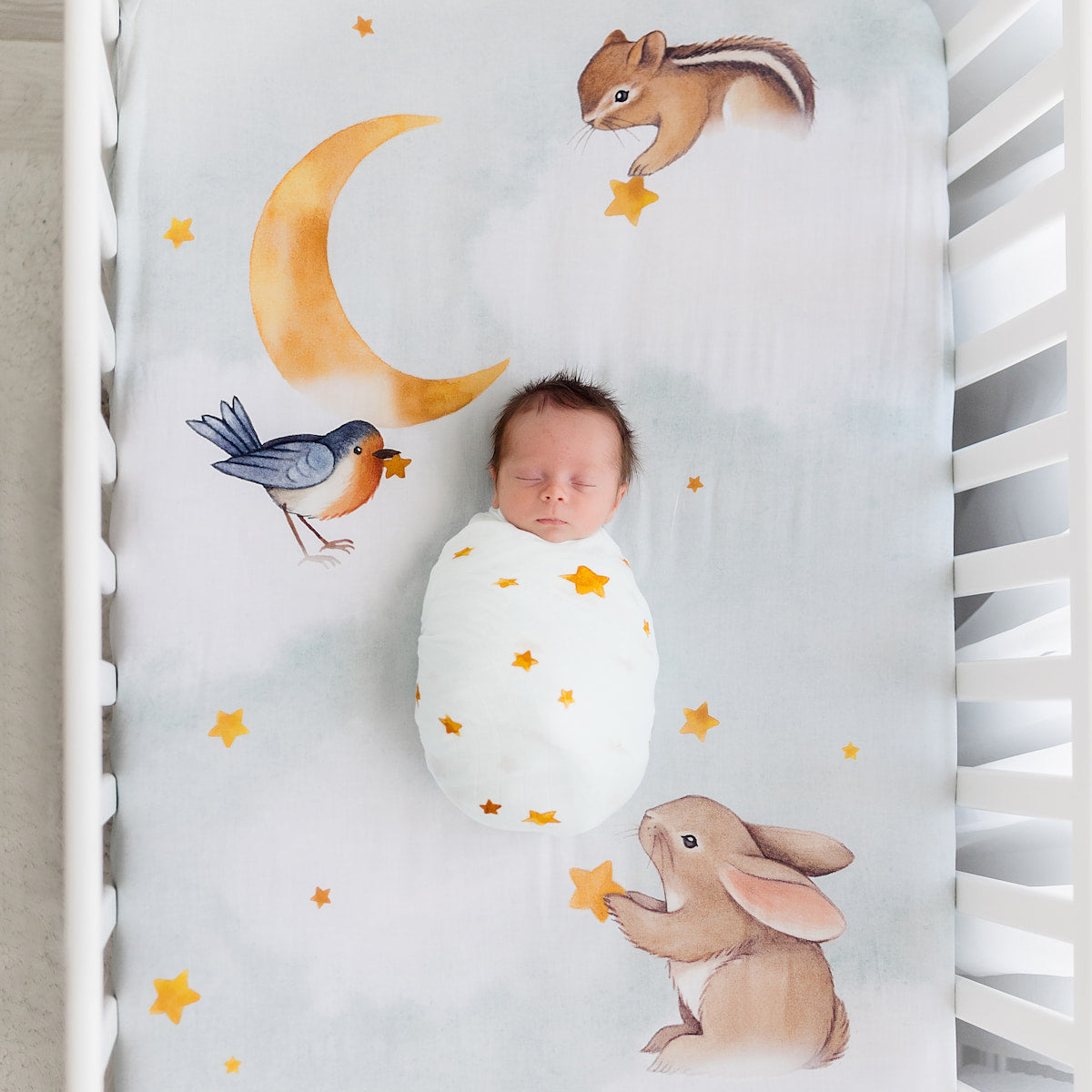 Newborn baby swaddled in a crib with animal illustrations on the sheet.