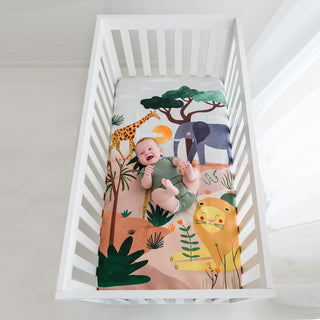 Baby lying on a crib with a colorful animal-themed blanket