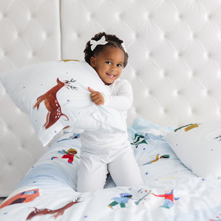 Child holding a pillow with animal designs on a bed with matching bedding.