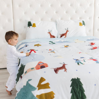 Child playing with a bedspread featuring animal prints on a bed.