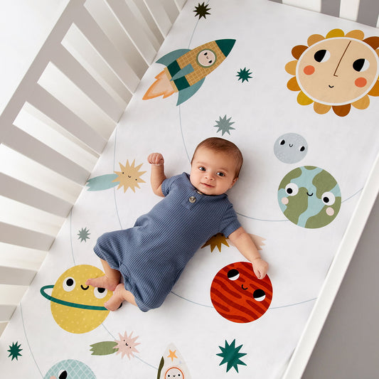 Baby lying on a crib sheet with space-themed illustrations