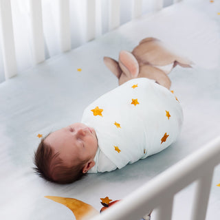 Newborn baby swaddled in a white blanket with star patterns, lying in a crib.
