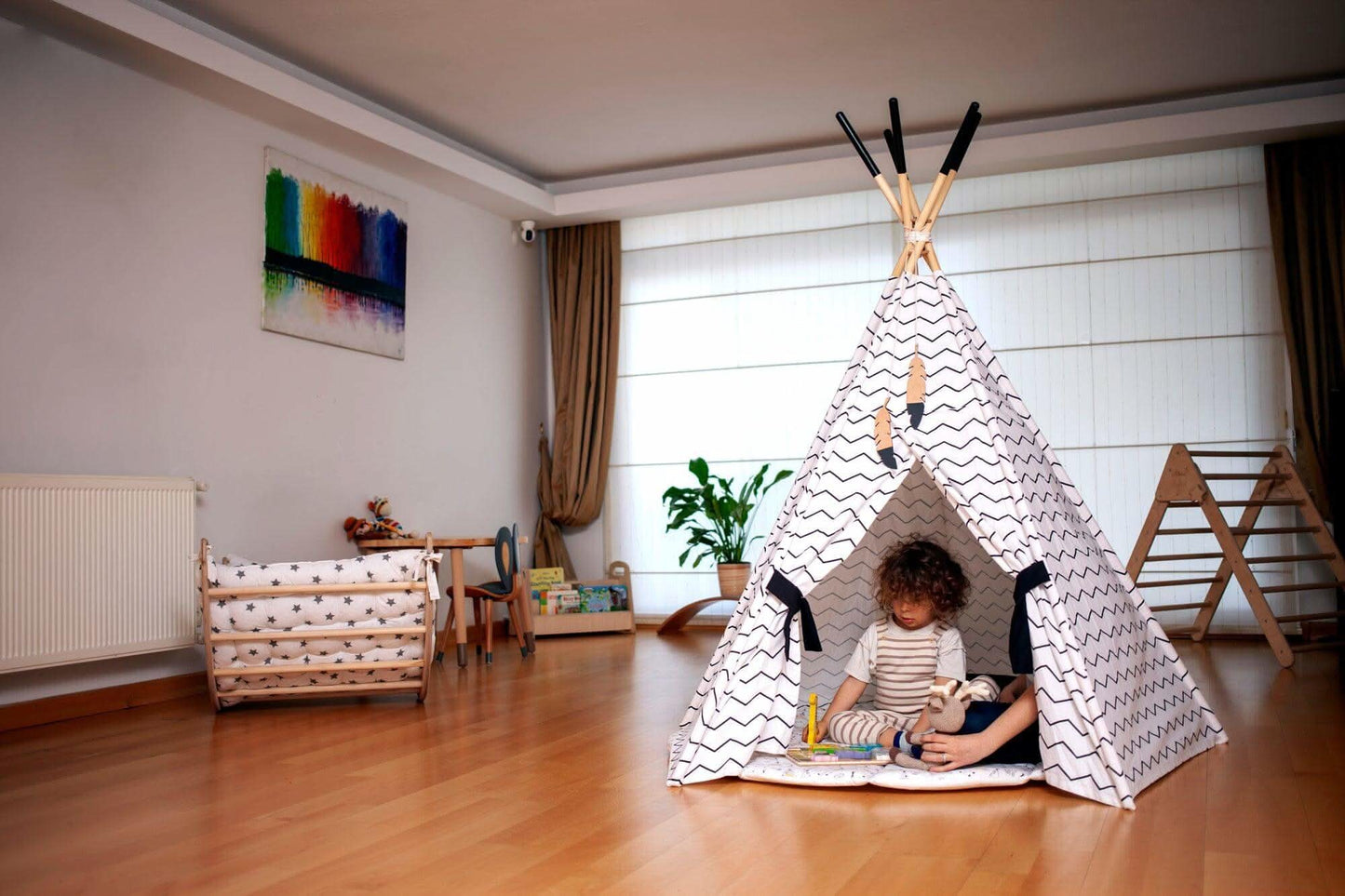 Child playing inside a teepee in a room with toys and furniture.